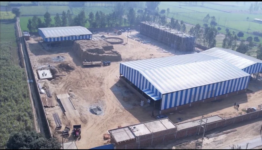 Aerial view of the Radha Raman Green Energy compressed bio-gas facility at Dhansri, Jansath, showing process halls and baled feedstock stacks